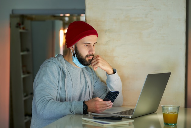 Un homme avec un masque facial travaillant sur son ordinateur portable