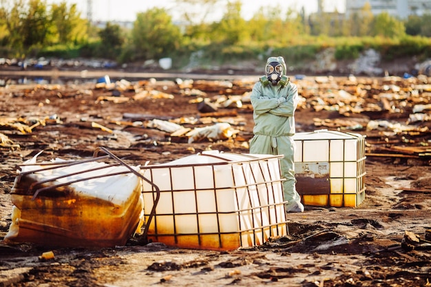 Un homme avec un masque à gaz et des vêtements militaires verts explore des barils après une catastrophe chimique