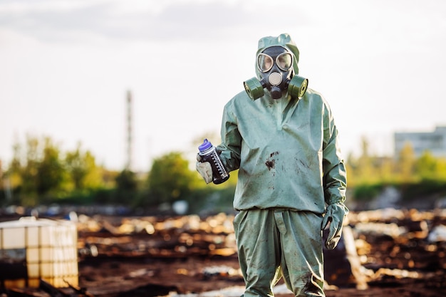 Un homme avec un masque à gaz et des vêtements militaires verts explore des barils après une catastrophe chimique