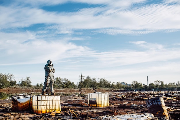 Un homme avec un masque à gaz et des vêtements militaires verts explore des barils après une catastrophe chimique