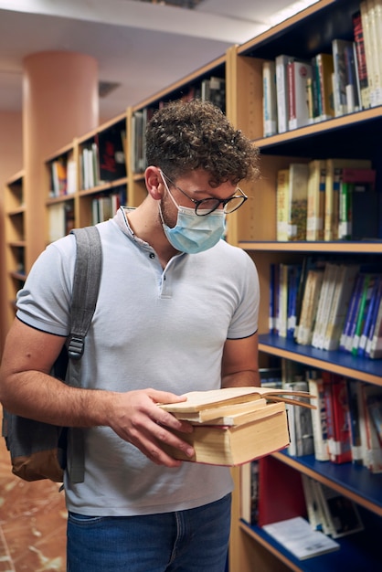 L'homme avec un masque lit des livres dans la bibliothèque universitaire