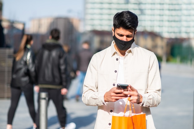 Homme masqué portant des sacs à provisions tout en utilisant un concept de smartphone, de covid et de coronavirus