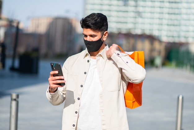 Homme masqué portant des sacs à provisions tout en utilisant un concept de smartphone, de covid et de coronavirus