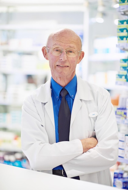 Homme mature pharmacien ou confiant dans le portrait pour l'expert des connaissances ou les soins de santé en pharmacie Chemiste sourire ou les bras croisés dans la pharmacie avec fierté carrière ou heureux pour le travail dans le dispensaire de détail