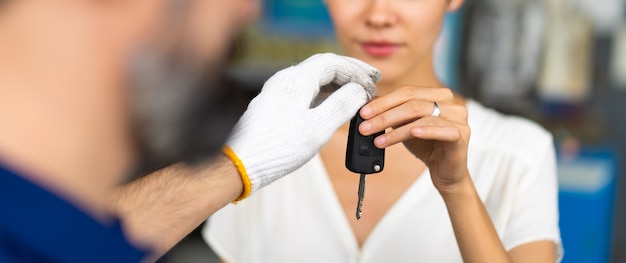 Homme mécanicien d'âge moyen avec barbe donne la clé de voiture à une cliente à la station d'entretien automobile et garage de service automobile