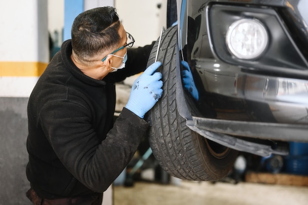 Homme mécanicien automobile avec masque facial travaillant dans un atelier de réparation automobile.