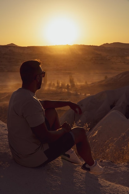 Homme méconnaissable appréciant le paysage de la vallée rouge au coucher du soleil avec les formations rocheuses typiques de la région de Cappadoce Turquie