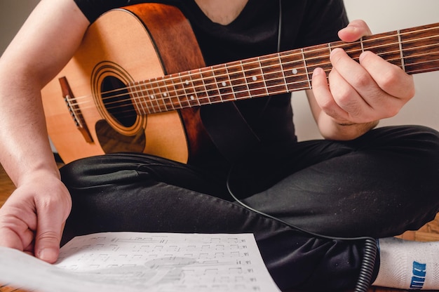 Homme méconnaissable assis sur le sol avec une guitare tenant des partitions dans sa main en gros plan