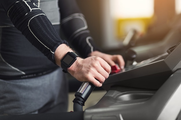 L'homme méconnaissable les mains sur les mains courantes du vélo elliptique dans le club de sport. Arrière-plan d'entraînement cardio, fonctionnant sur tapis roulant. Mode de vie sain, entraînement de gars en salle de sport, vue latérale, espace de copie