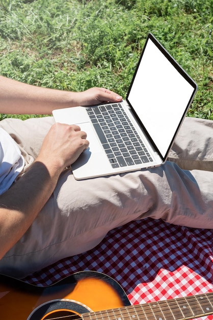 Homme méconnaissable en pantalon blanc à l'extérieur en train de pique-niquer et utilisant un ordinateur portable travaillant à l'extérieur