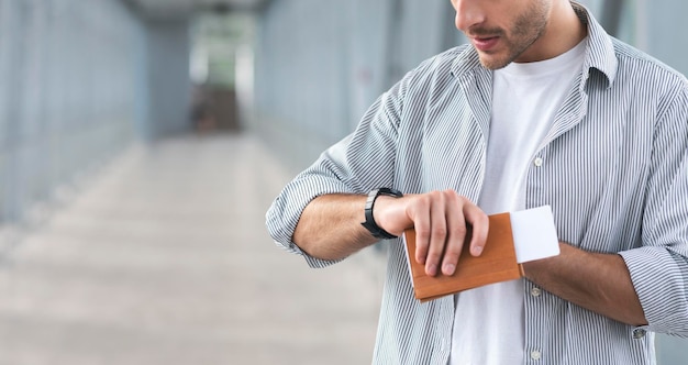 Homme méconnaissable tenant un passeport et des billets et vérifiant l'heure à la montre-bracelet