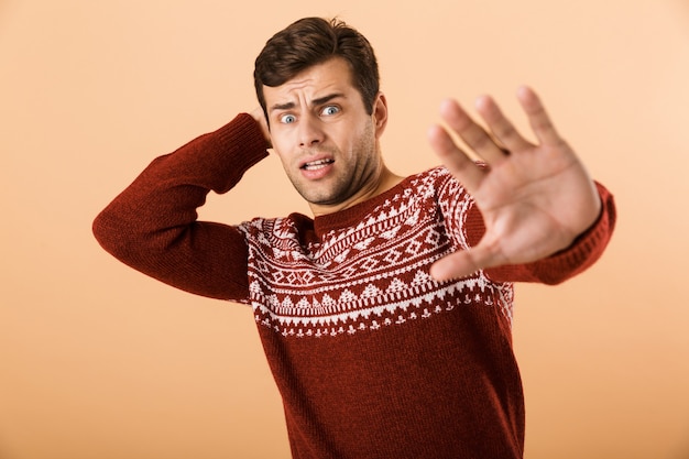 Photo homme mécontent avec chaume portant chandail tricoté faisant le geste d'arrêt avec les mains, isolé sur mur beige