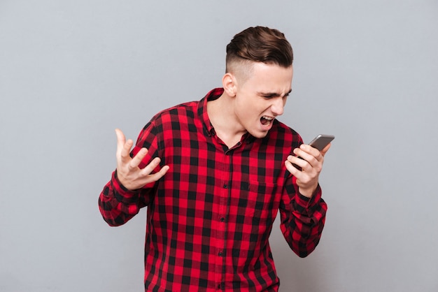 Homme mécontent en chemise criant au téléphone. Fond gris isolé