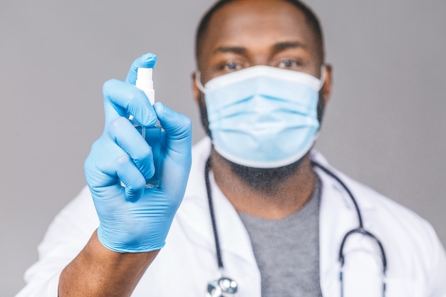 Homme médecin afro-américain en gants de masque de robe. Bouteille de désinfectant antibactérien liquide.