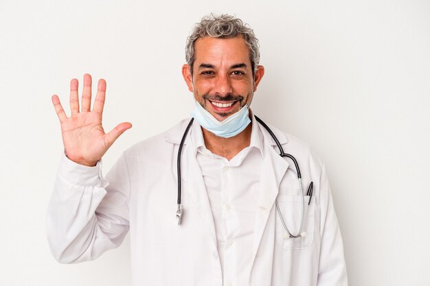 Homme médecin d'âge moyen portant un masque pour virus isolé sur fond blanc souriant joyeux montrant le numéro cinq avec les doigts.