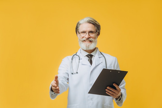 Homme médecin aux cheveux gris portant stéthoscope debout sur un mur jaune isolé