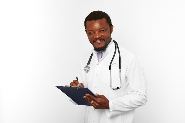 Homme médecin barbu noir souriant en robe blanche avec stéthoscope remplissant les dossiers médicaux sur le presse-papiers
