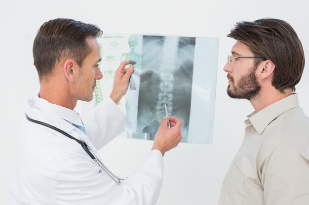 Homme médecin expliquant la radiographie de la colonne vertébrale au patient