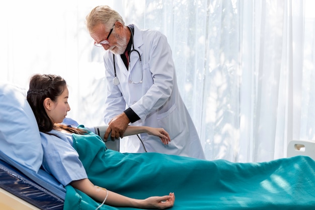 Homme médecin professionnel caucasien senior vérifier la pression artérielle avec une patiente asiatique dans la chambre d'hôpital.