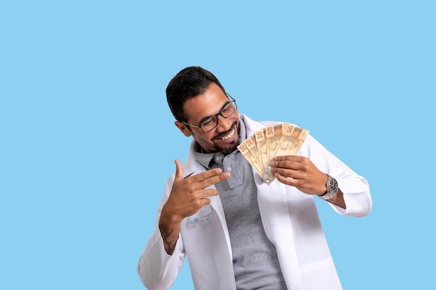 homme médecin tenant de l'argent brésilien souriant joyeusement, homme tenant de l'argent, portant un uniforme blanc, santé