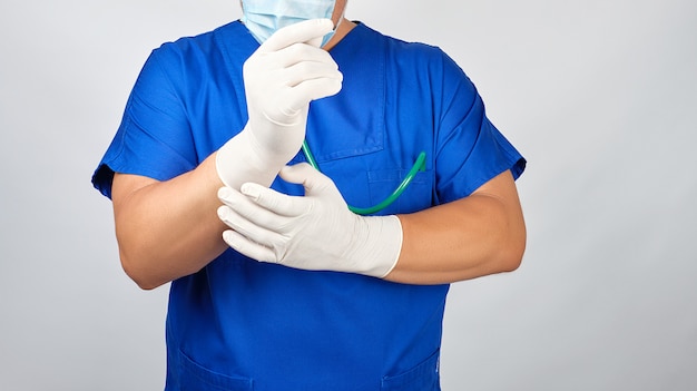 Homme médecin en uniforme bleu met sur ses mains des gants en latex stériles blancs