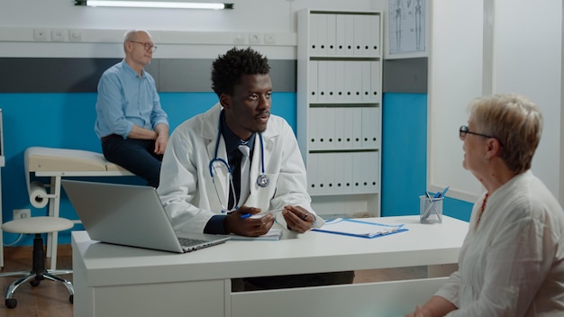 Homme médecin en uniforme faisant des consultations pour un patient retraité âgé assis au bureau. Jeune médecin discutant avec une femme aînée dans un cabinet de soins de santé avec des instruments médicaux