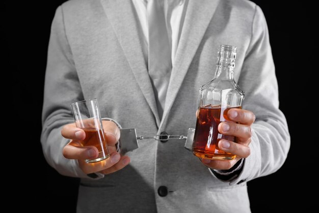 Photo homme menotté avec bouteille et verre de cognac sur fond sombre concept de dépendance à l'alcool