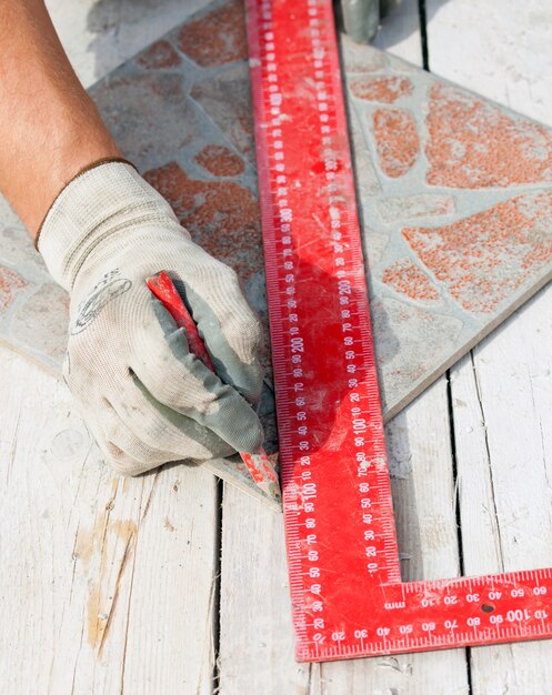 Homme mesurant une pièce de tuile avec un crayon