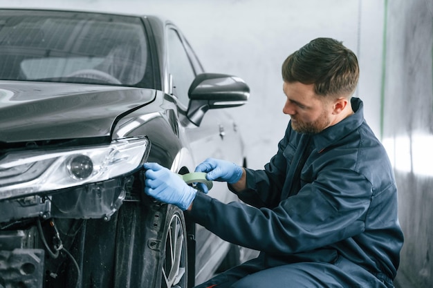 L'homme met du ruban adhésif sur la surface cassée de l'automobile