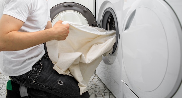 L'homme met le linge dans une machine à laver automatique