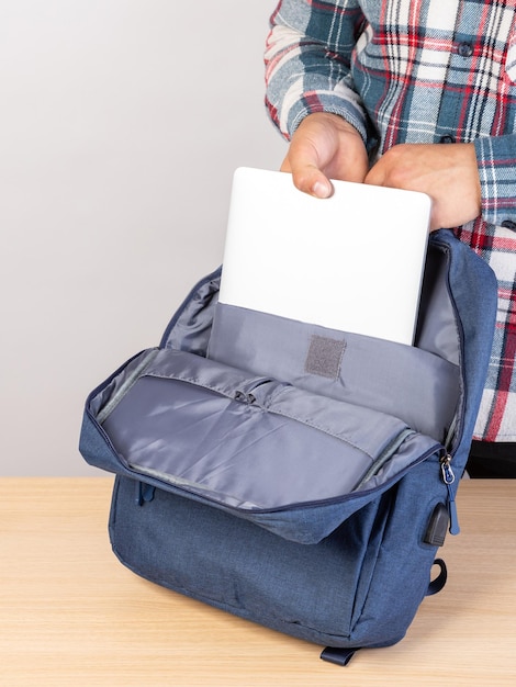 Un homme met un ordinateur portable dans un sac à dos à l'extérieur sur un fond clair Un jeune homme met un ordinateur portable dans un sac à dos Un homme sort un ordinateur portable de son sac à dos