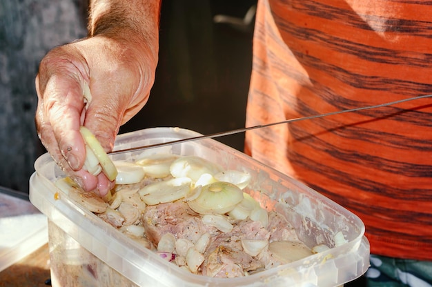 Un homme met de la viande marinée et des oignons sur une brochette gros plan Barbecue shish kebab cuisson