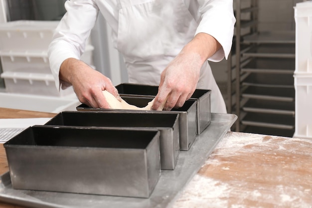 Homme mettant de la pâte sous forme métallique sur une table dans une boulangerie