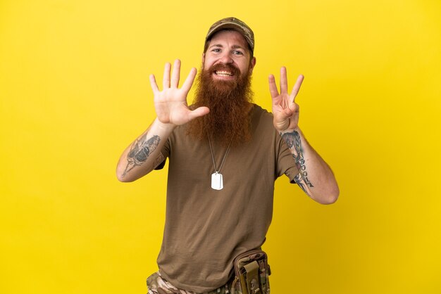 Homme militaire rousse avec dog tag isolé sur fond jaune comptant huit avec les doigts