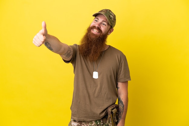 L'homme militaire rousse avec dog tag isolé sur fond jaune donnant un coup de pouce geste