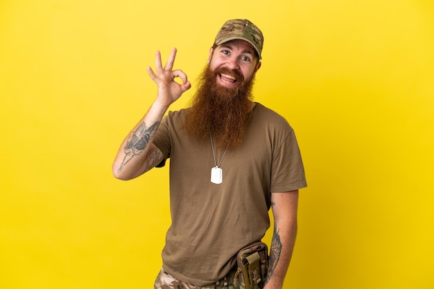 Homme militaire rousse avec dog tag isolé sur fond jaune montrant un signe ok avec les doigts