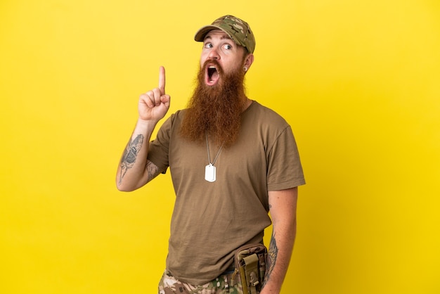 Homme militaire rousse avec dog tag isolé sur fond jaune pensant une idée pointant le doigt vers le haut