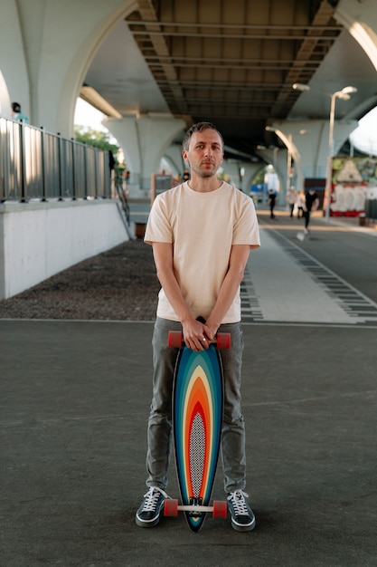 Un homme millénaire tient une planche à roulettes ou un longboard à l'intérieur dans un espace urbain pour des entraînements de patinage extrême