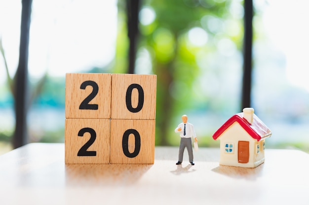 Homme miniature debout avec mini maison et année 2020 dans des blocs de bois