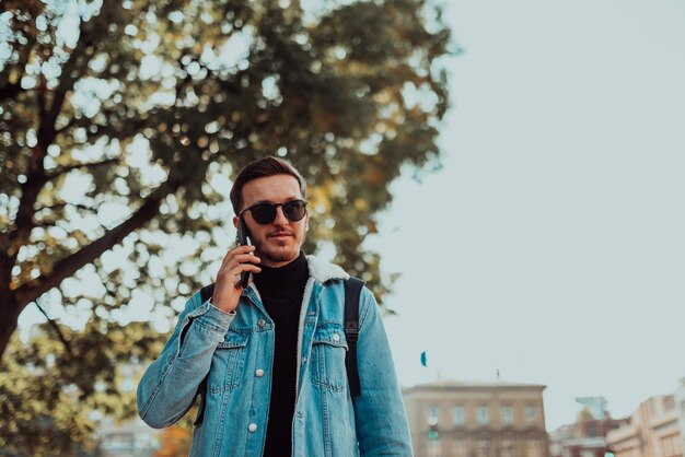 Homme moderne à lunettes de soleil parlant sur le smartphone dans la rue