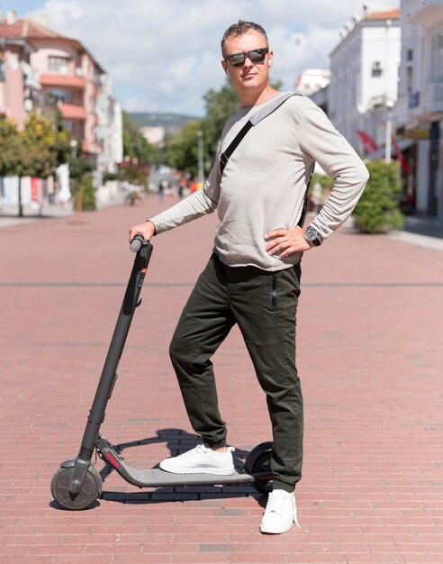 Homme moderne avec des lunettes de soleil posant sur scooter