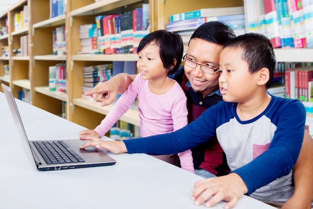 Homme montrant à ses enfants comment utiliser un ordinateur portable dans la bibliothèque