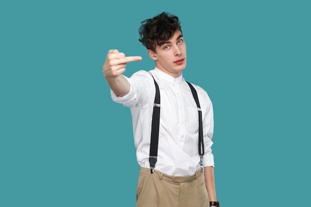 Homme montrant le signe du doigt du milieu et regardant la caméra. Portrait de beau jeune homme d'affaires bouclé hipster en chemise blanche décontractée classique et jarretelle. tourné en studio isolé sur fond bleu.