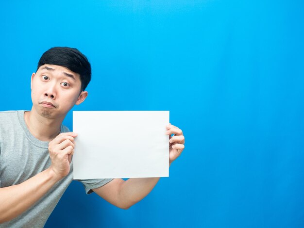 L'homme montre une feuille blanche vide sur fond bleu à la main