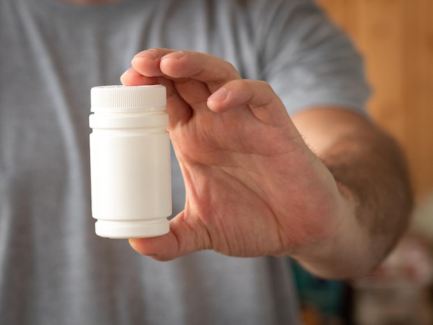 L'homme montre un pot blanc avec des médicaments ou des multivitamines.