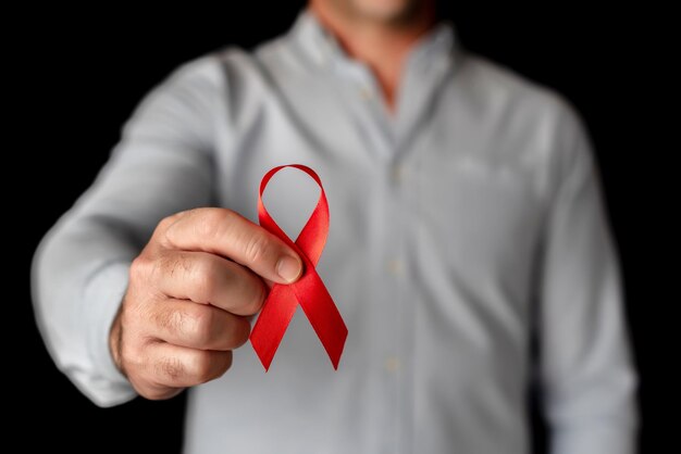 Un homme montre un ruban rouge à l'appui de la Journée mondiale du sida sur fond noir Lutte contre le virus VIH