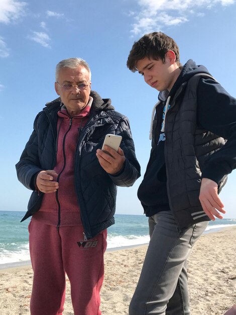 Photo un homme montre son téléphone portable à son petit-fils alors qu'il se tient sur la plage.