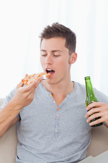 Un homme avec un morceau de pizza et de la bière dans ses mains