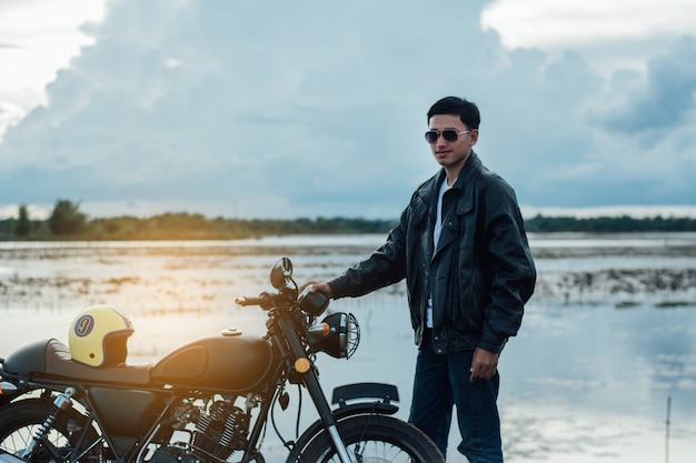 Homme motard avec sa moto au bord du lac naturel et magnifique.