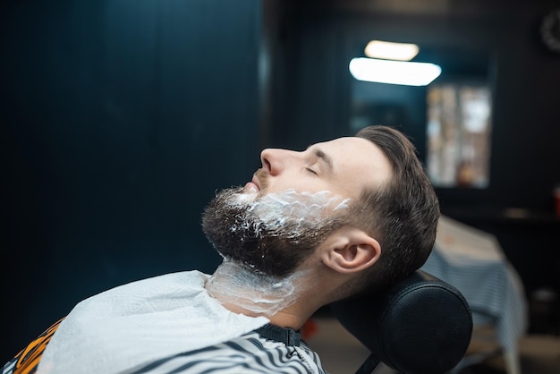 Homme avec de la mousse à raser sur son visage dans un salon de coiffure vue rapprochée